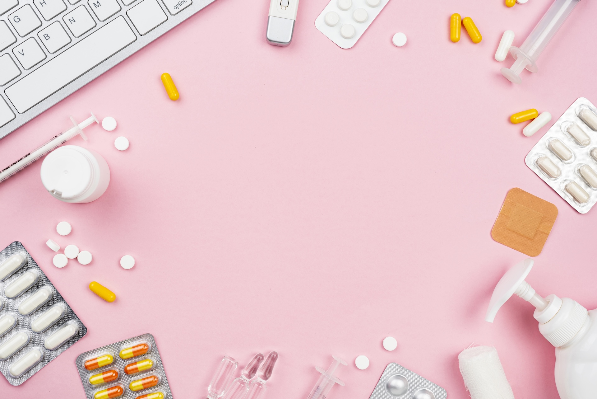 médicaments et clavier d'ordinateurs posé sur un bureau rose