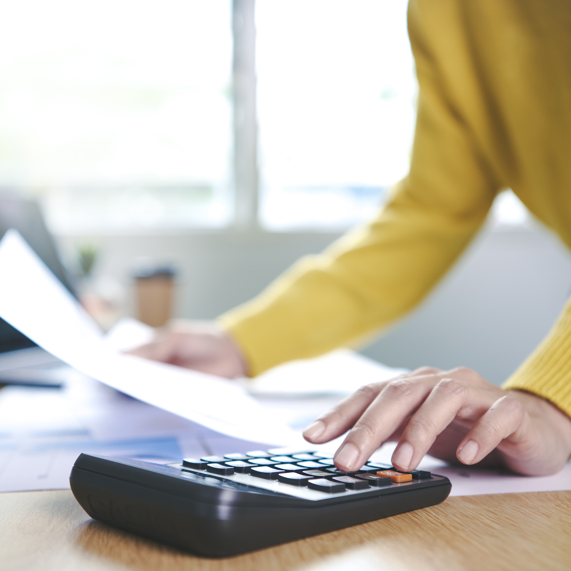 Femme qui effectue un calcul avec une main sur une calculatrice et tenant un bulletin de paye dans l'autre main