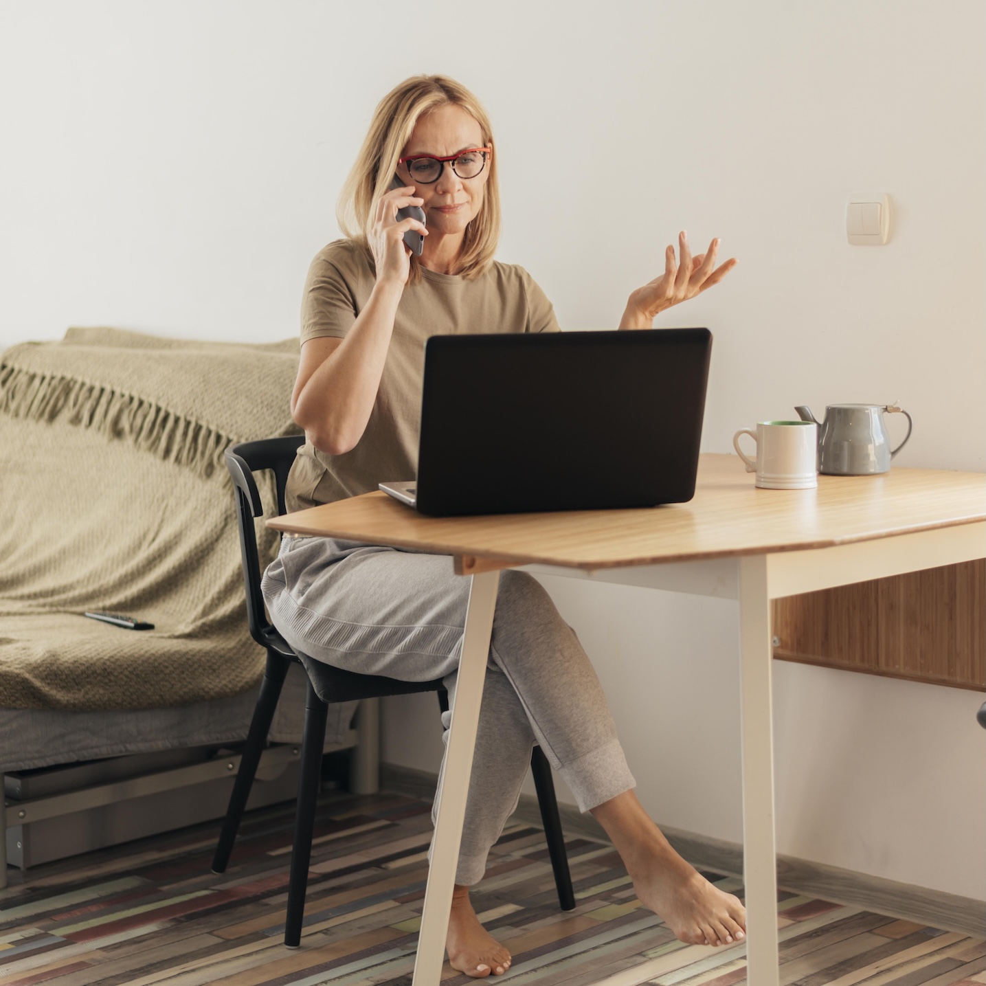 Femme en télétravail chez elle face à son ordinateur portable, qui est au téléphone