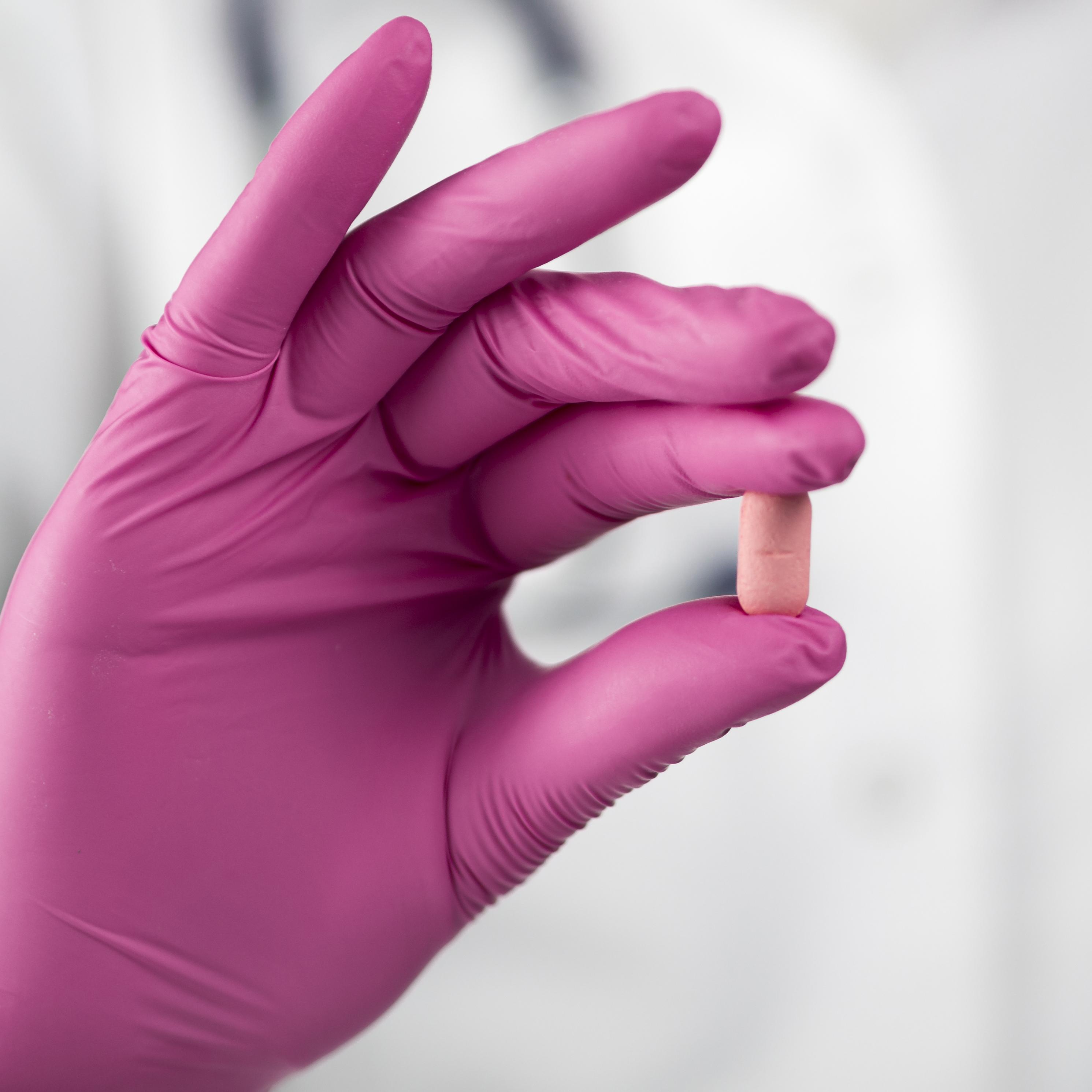 Main dans un gant médical rose qui tient un médicament rose pour illustrer la pharmacovigilance